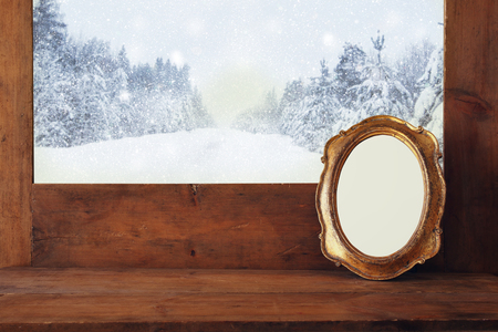 Golden old blank frame on wooden window sill and winter snowy landscapeの写真素材