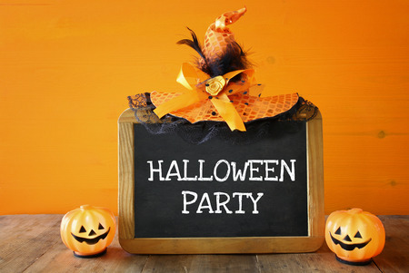 Halloween holiday concept. Witch hat, cute pumpkin next to blackboard with text: HALLOWEEN PARTY, on wooden tableの写真素材