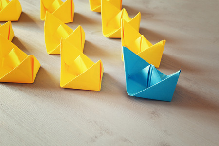 Leadership concept with paper boats on blue wooden background. One leader ship leads other ships. Filtered and toned imageの写真素材