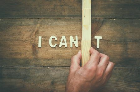 Man hand building the wall between letters I CAN'T, cutting the letter T so it written I CAN....