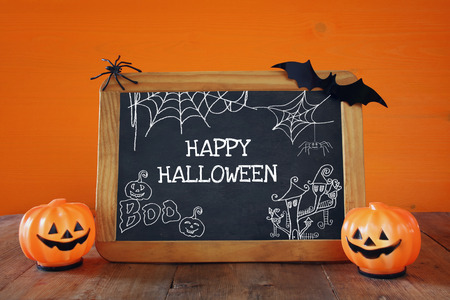 Halloween holiday concept. Cute pumpkins next to blackboard with hand made illustrations, on wooden tableの写真素材