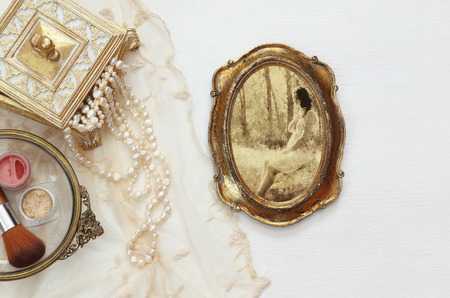 Top view image of vintage woman toilet fashion objects next to photo frame with photography of beautiful woman on wooden tableの写真素材