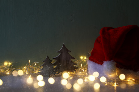 Low key Image of wooden christmas tree with garland warm lights next to santa hatの写真素材