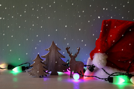 Low key Image of wooden christmas tree and deer with garland colorful lights next to santa hatの写真素材