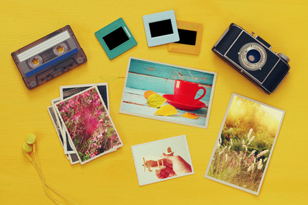 Top view of photographs next to old camera over yellow wooden table. Flat layの写真素材