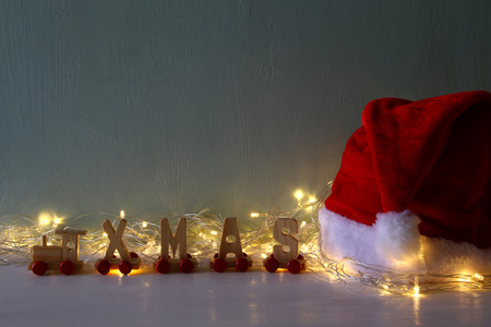 Low key Image of warm garland lights next to santa hat and wooden letters spelling word: XMASの写真素材