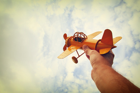 close up photo of man's hand holding retro airplane against blue sky. Filtered imageの写真素材