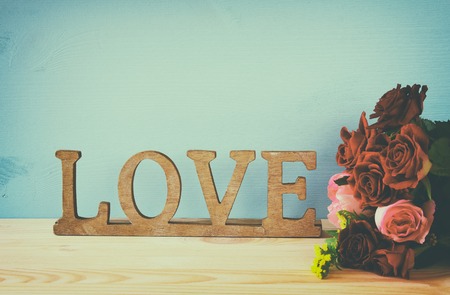Valentines day background. Word LOVE from wooden letters next to beautiful bouquet of roses on old table. Filtered and tonedの写真素材