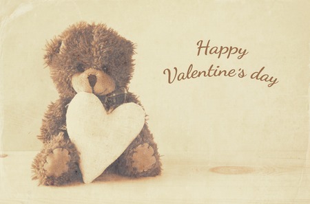 Valentines day concept. Cute teddy bear sitting and holding a heart, on wooden table. Sepia style filterの写真素材