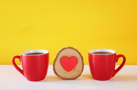 Wooden heart next to coffee cups on wooden table.の写真素材
