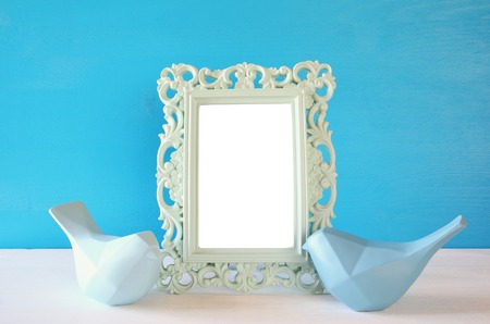 Couple of Lovebirds and blank photo frame on wooden table in front of blue pastel background. Ready to put photographyの写真素材