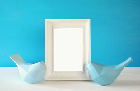Couple of Lovebirds and blank photo frame on wooden table in front of blue pastel background. Ready to put photographyの写真素材