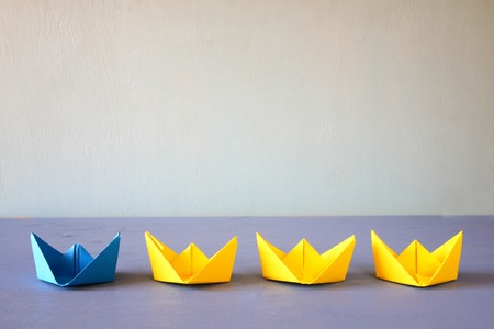Leadership concept with paper boats on blue wooden background. One leader ship leads other ships. Filtered and toned imageの写真素材