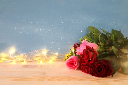 Valentines day background. Beautiful bouquet of roses next to gold garland lifhgs on wooden tableの写真素材