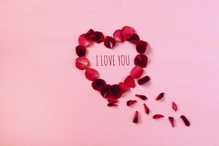 Top view of red rose petals making heart shape on pastel pink backgroundの写真素材
