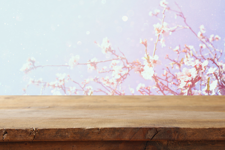 wooden rustic table in front of spring white cherry blossoms tree. vintage filtered image. product display and picnic conceptの写真素材