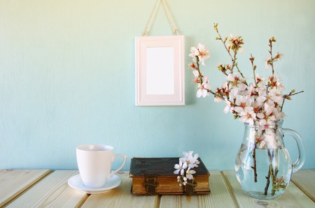 old book, cup of coffee next to spring white flowers on wooden tableの写真素材
