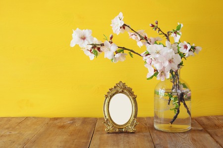 Vintage blank photo frame next to spring white flowers on wooden tableの写真素材