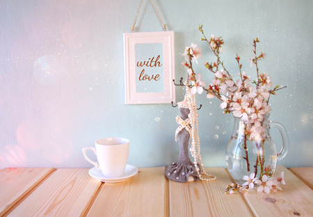 vintage jewelery stand with pearls necklace, blank frame next to white spring flowers on wooden tableの写真素材