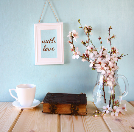 old book, cup of coffee next to spring white flowers on wooden tableの写真素材