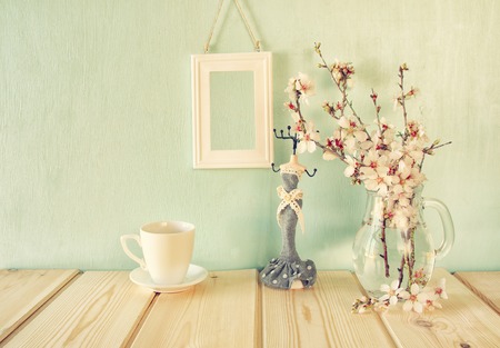 vintage jewelery stand with pearls necklace, blank frame next to white spring flowers on wooden tableの写真素材