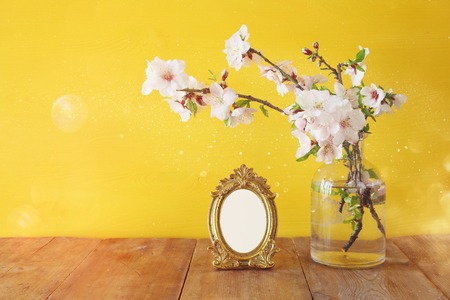 Vintage blank photo frame next to spring white flowers on wooden tableの写真素材