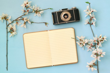 top view image of spring white cherry blossoms tree, open blank notebook, old camera on wooden tableの写真素材