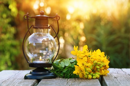 Vintage oriental lantern and yellow spring field flowers over wooden table outdoors in the garden at sunset light. Filtered imageの写真素材