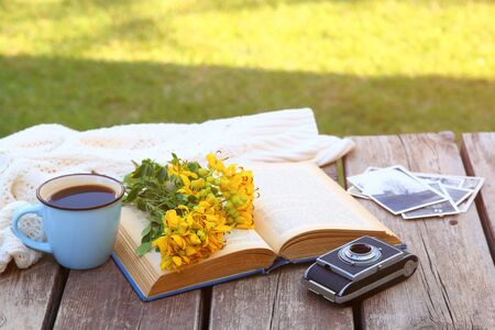 old book, vintage photo camera next to field flowers on wooden table outdoors at afternoon. selective focusの写真素材