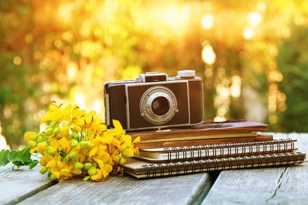 Image of notebooks next to vintage photo camera on wooden table outdoors at afternoon. selective...