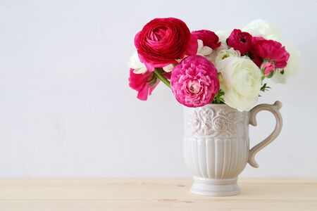 Bouquet of pink and white rosses in the vintage white vase on wooden table