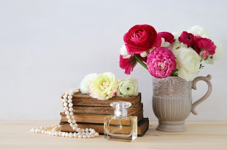 Beautiful bouquet of spring flowers in the vase next to old books, pearls necklace and perfume...