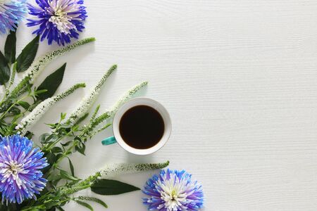 Top view image of cup of coffee and beautiful blue and white flowers arrangement on wooden backgroundの写真素材