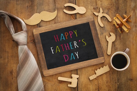 top view image of fathers day composition with wooden shape tools, necktie , cup of coffee and blackboard on wooden background. Father's day conceptの写真素材
