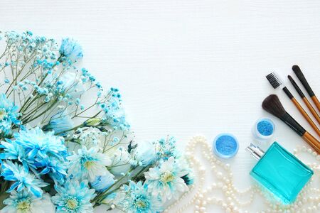 Top view of beautiful and delicate blue flowers arrangement next to pearls necklace, fresh perfume and makeup on white wooden background. Copy spaceの写真素材