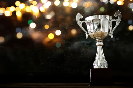 low key image of trophy over wooden table and dark background, with abstract glitter lightsの写真素材