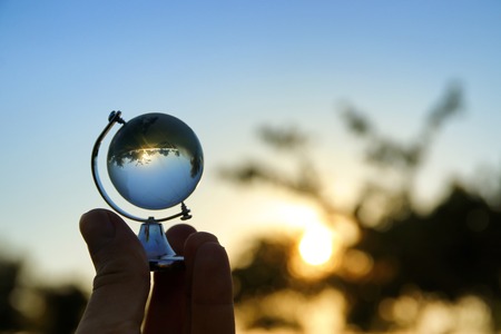 male hand holding small crystal globe in front of sunset. travel and global issues conceptの写真素材