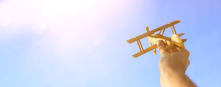 close up photo of man's hand holding toy airplane against sunset skyの写真素材