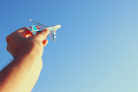 close up photo of man's hand holding toy airplane against blue skyの写真素材