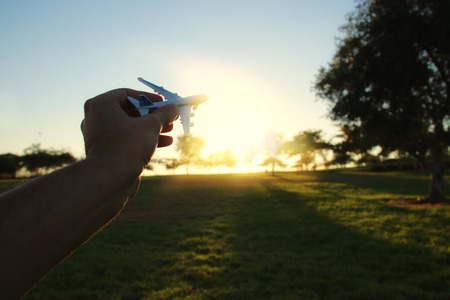 close up photo of man's hand holding toy airplane against sunset sky