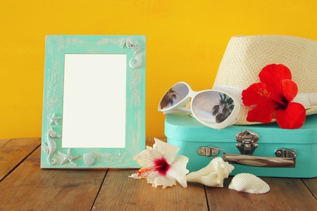 Fedora hat, sunglasses, tropical hibiscus flower next to blank frame over wooden table. relaxation or vacation concept. For photography montageの写真素材