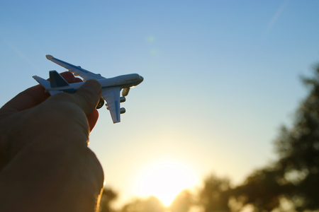 close up photo of man's hand holding toy airplane against sunset skyの写真素材