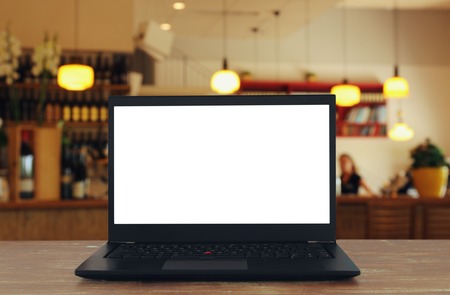 Image of open laptop with white screen on wooden table in front of abstract blurred restaurant...