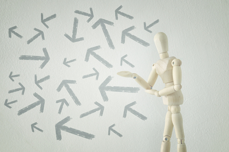 image of wooden person standing with his back in front of textured background full of arrows pointing in different directions. decision and strategy plan conceptの写真素材