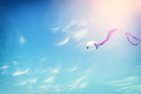 Colorful kite flying in the blue sky through the clouds.の写真素材