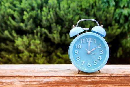 Image of autumn Time Change. Fall back concept. Dry leaves and vintage alarm Clock on wooden table outdoors at afternoonの写真素材