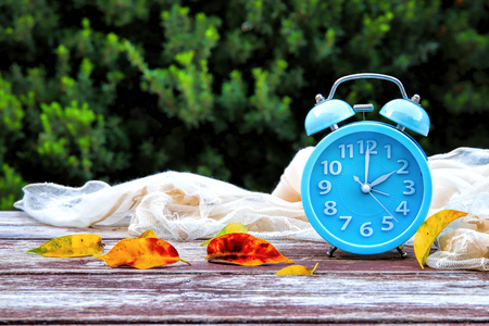 Image of autumn Time Change. Fall back concept. Dry leaves and vintage alarm Clock on wooden table outdoors at afternoonの写真素材