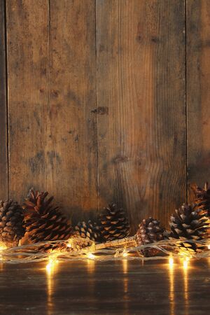 Holiday image with Christmas golden garland lights and pine cones over wooden background.