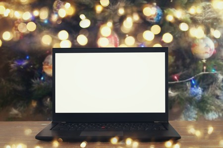 Image of open laptop with white screen on wooden table in front of christmas tree background. For mockupの写真素材