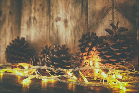 Holiday image with Christmas golden garland lights and pine cones over wooden background.の写真素材